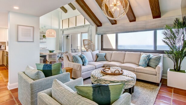 A spacious living room with a large beige sectional sofa, a coffee table, and a dining area with a white table and chairs.