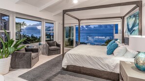 A modern bedroom with a large bed, a view of the ocean, and a balcony with seating.