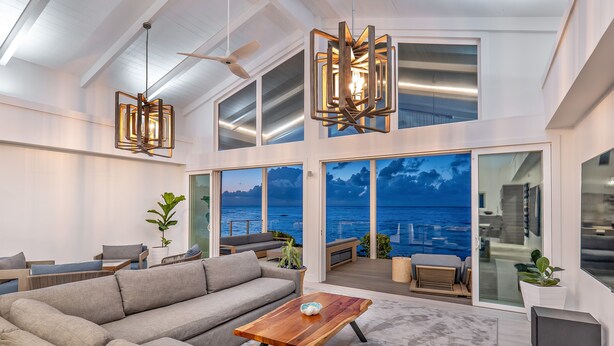 A spacious living area with a large sofa, a wooden coffee table, and a view of the ocean through large windows.