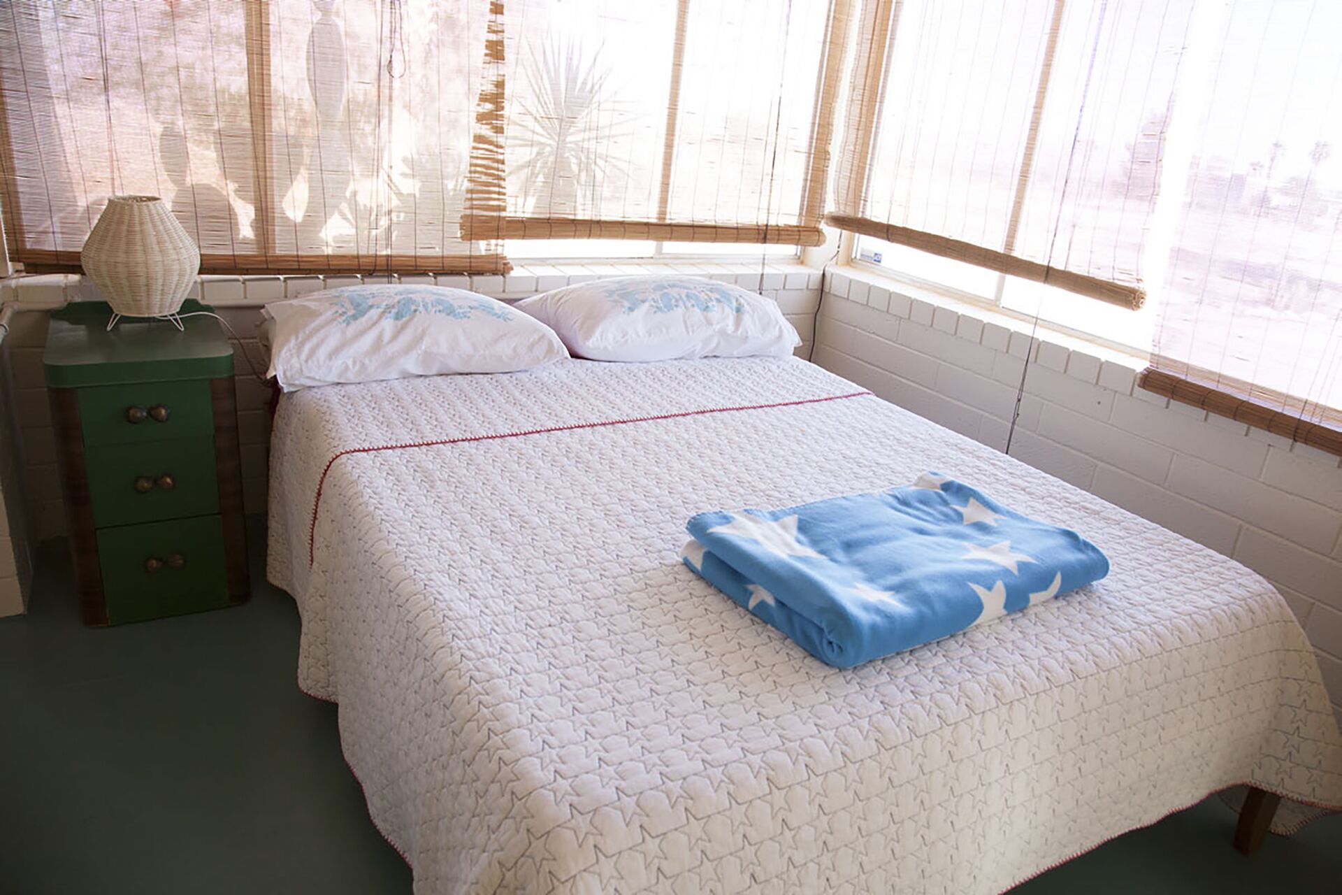 A neatly made bed with a quilted pattern, a blue blanket, and a bedside lamp on a green nightstand.
