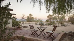 An outdoor patio with a table and four chairs, surrounded by a garden with various plants and a view of a desert landscape. - Midcentury Desert Escape (Twentynine Palms)