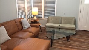 Ett vardagsrum med en brun lädersoffa, ett soffbord i glas, en beige soffa och en lampa på ett sidobord.