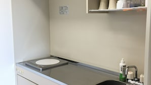 A kitchenette with a stove, sink, and storage cabinets. - Pension Sakae Club (Nanjo)