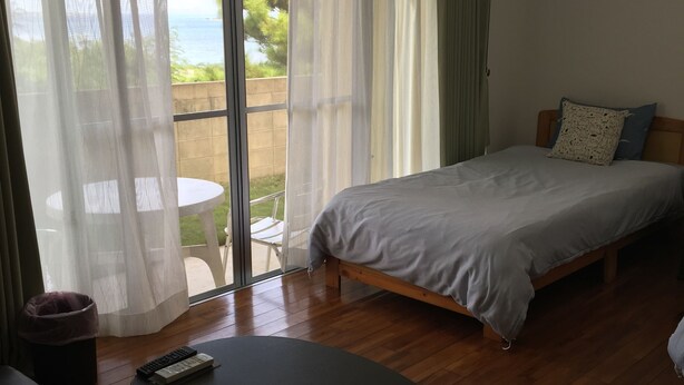 A bedroom with a bed, a sofa, a table, and a view of the outdoors. - Pension Sakae Club (Nanjo)