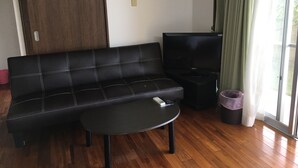 A living room with a black sofa, a black coffee table, a television, and a sliding glass door with curtains. - Pension Sakae Club (Nanjo)