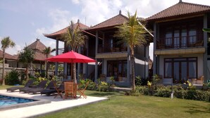 A resort with a swimming pool, lounge chairs, and a red umbrella. - Khalisha Villa (Mendoyo)