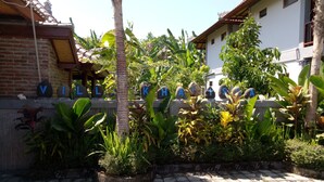 A courtyard with a paved walkway, surrounded by lush greenery and a building with a tiled roof. - Khalisha Villa (Mendoyo)