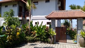 A two-story house with a tiled roof, a gated entrance, and lush tropical plants. - Khalisha Villa (Mendoyo)