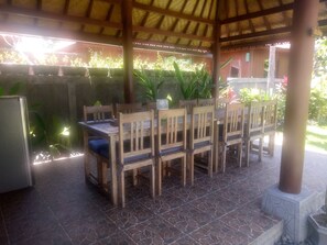 An outdoor patio with a wooden table and chairs, surrounded by potted plants and a tiled floor. - Khalisha Villa (Mendoyo)