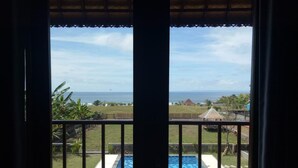 A view from a balcony with a pool, ocean, and tropical vegetation. - Khalisha Villa (Mendoyo)