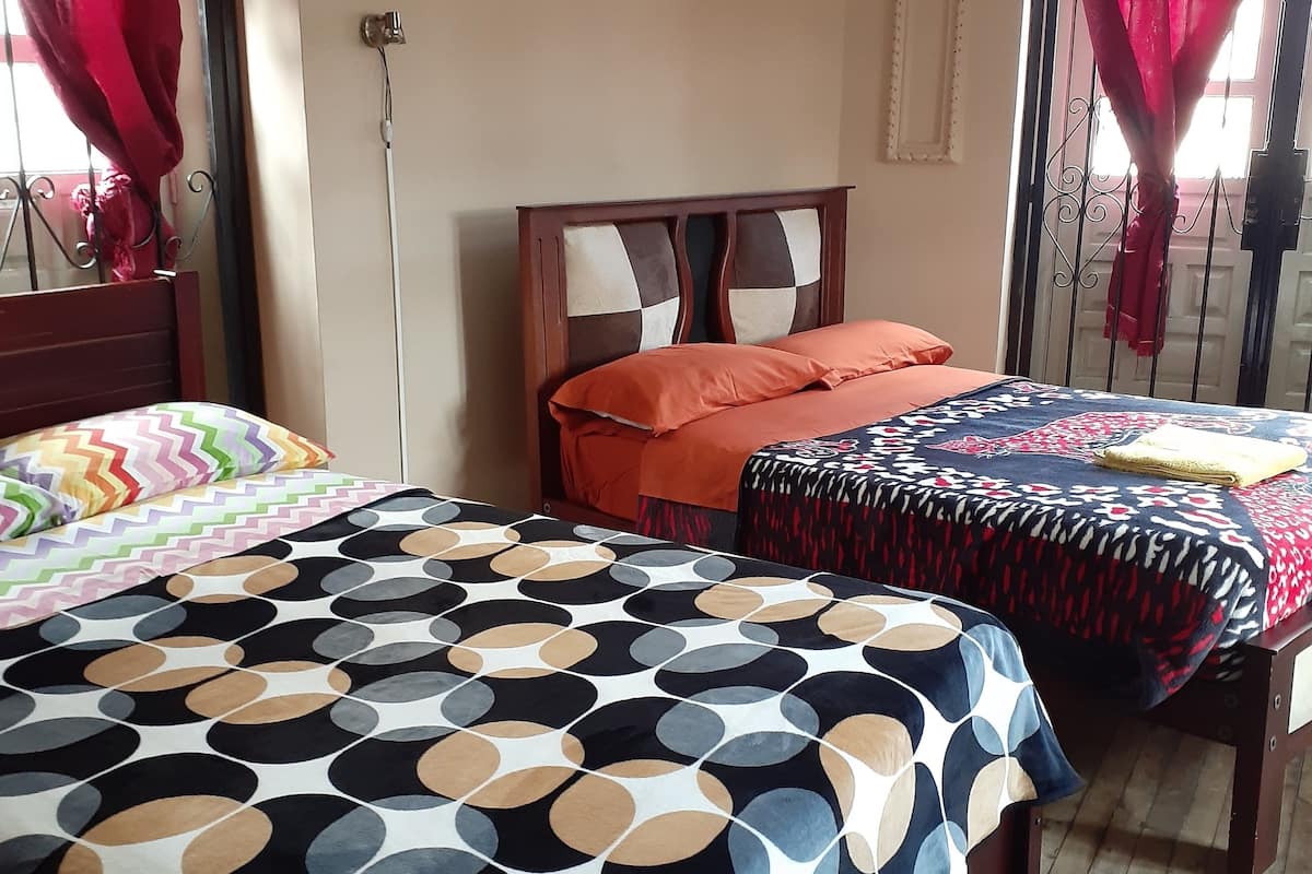A bedroom with two beds, each with patterned bedding, a wooden headboard, and a window with curtains.