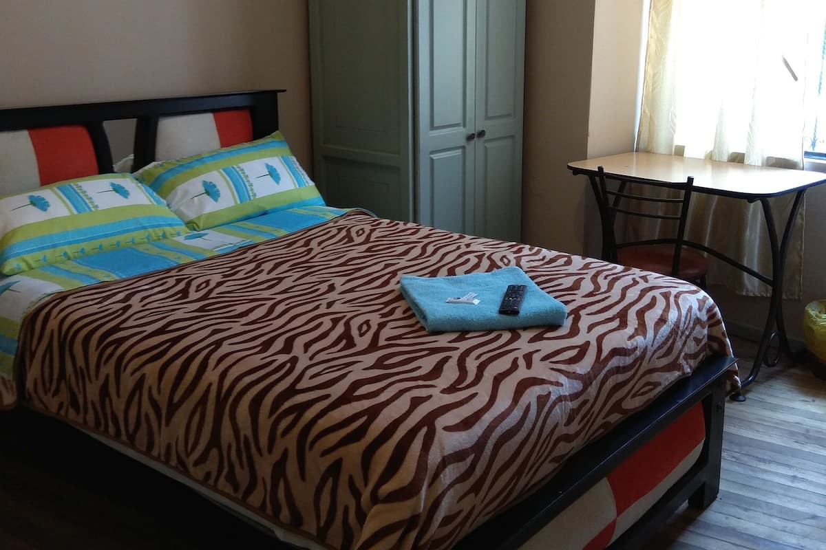 A bedroom with a bed, a wardrobe, a table, and a window with curtains.