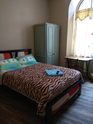 A bedroom with a bed, a wardrobe, a table, and a window with curtains. - Hostal Mediodía (Quito)