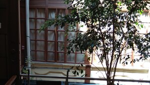 A small indoor area with a potted tree, a glass table with a laptop, and a window with a view of a building. - Hostal Mediodía (Quito)