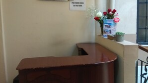 A reception desk with a sign above it, a window with a view of a snowy landscape, and a small potted plant with flowers on the desk. - Hostal Mediodía (Quito)