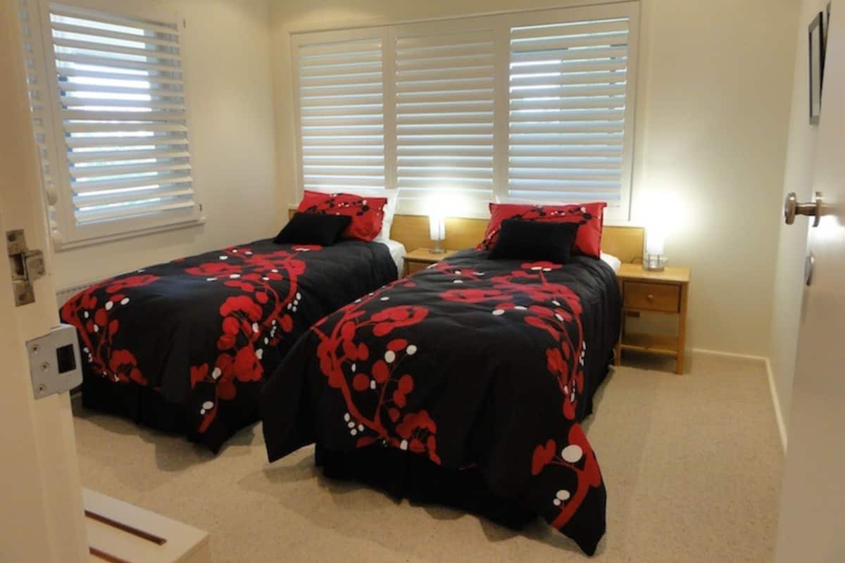 Ein Schlafzimmer mit zwei Betten, jeweils mit schwarz-roter Blumenbettwäsche, weißen Jalousien an den Fenstern und Nachttischlampen.