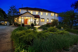 A two-story house with a well-lit front porch and a garden in front.