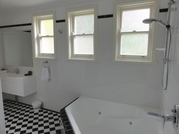 A bathroom with a checkered floor, a bathtub, a sink, and three windows.