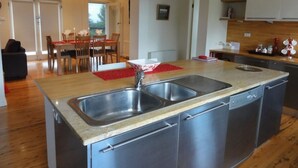 Une cuisine moderne dotée d’un îlot central, d’appareils électroménagers en acier inoxydable et d’un coin repas avec des chaises en bois et un chemin de table rouge.