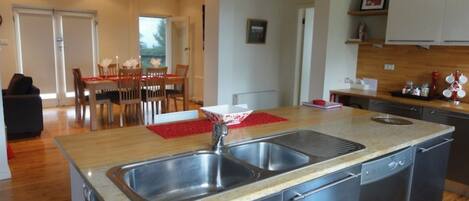 A modern kitchen with a central island, stainless steel appliances, and a dining area with wooden chairs and a red table runner.
