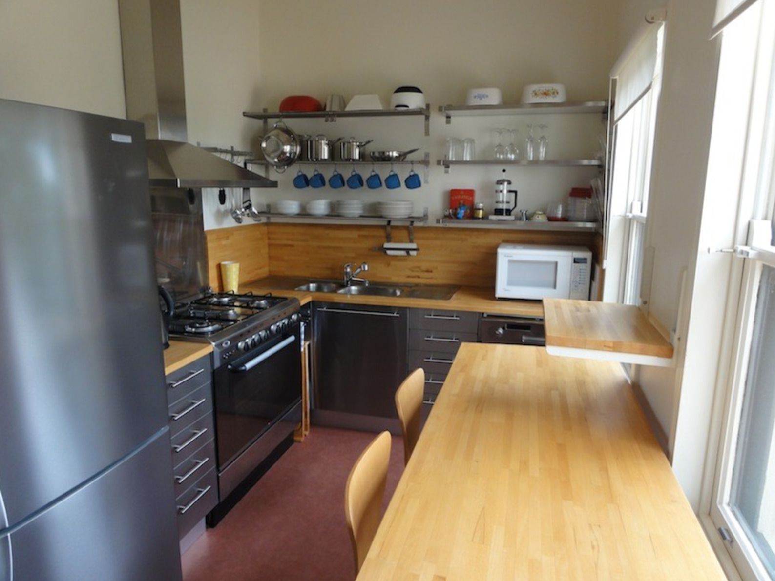Una cucina compatta con frigorifero, piano cottura, microonde e tavolo in legno.