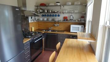 A compact kitchen with a refrigerator, stove, microwave, and wooden table.