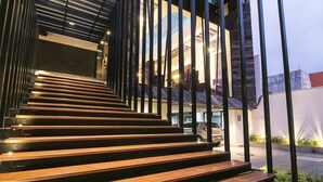 Una escalera de madera con barandas metálicas que lleva a la entrada de un edificio moderno.
