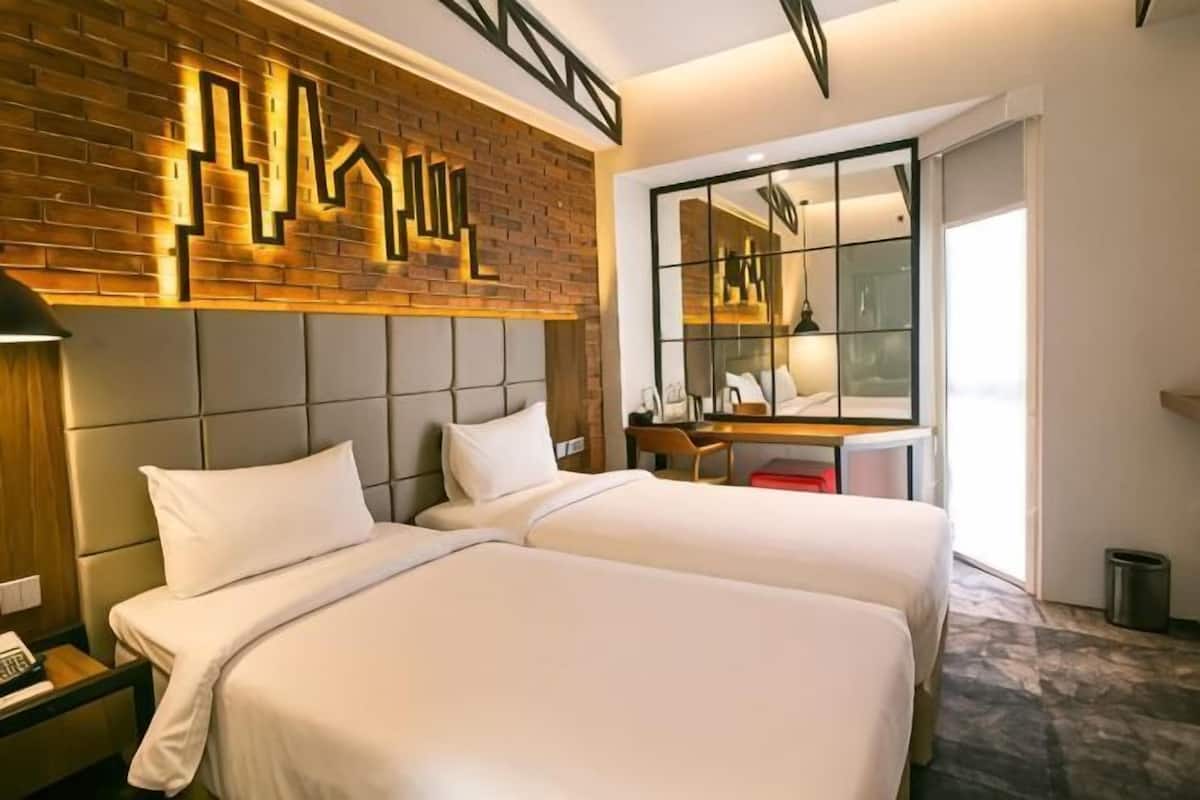 Een hotelkamer met twee bedden, een wand van baksteen, een grote spiegel en een bureau met stoel.