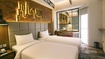 Habitación de hotel con dos camas, un escritorio, un espejo y una pared de ladrillo decorativa.