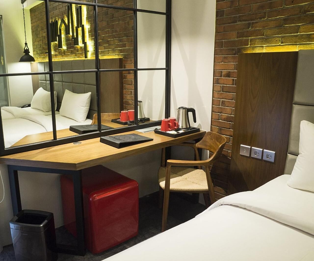A hotel room with a wooden desk, a chair, a bed, and a mirror reflecting the room.