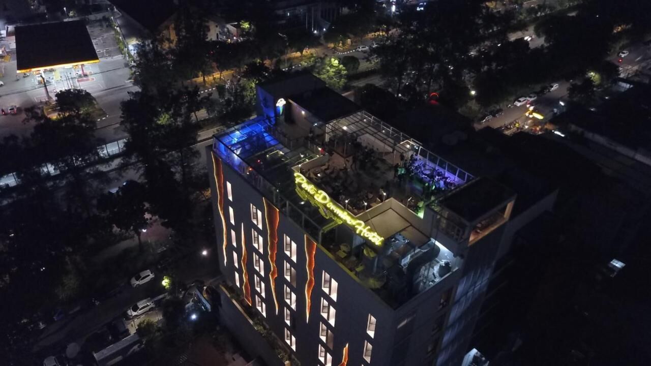 Un hotel de varios pisos con terraza en la azotea, piscina e iluminación exterior.