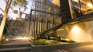 Un edificio moderno con una escalera, un muro de piedra y un jardín con fuente.