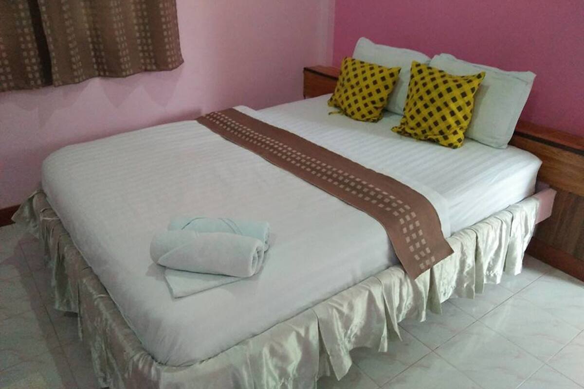 Una cama bien hecha con una colcha blanca, dos almohadas con un estampado amarillo y un ribete decorativo marrón.