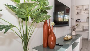 Een moderne woonkamer met een flatscreen televisie aan de muur, een glazen salontafel en een kamerplant.