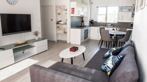 Een moderne woonkamer met een flatscreen televisie, een grijze bank en een eethoek met een tafel en stoelen.