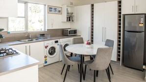 Een moderne keuken met een spoelbak, magnetron, wasmachine en een eethoek met stoelen en een tafel.