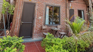 Une maison en briques avec un toit en tuiles, une porte et des fenêtres. On y trouve une petite terrasse avec une table et des chaises.