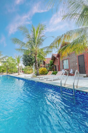 A swimming pool with clear blue water, surrounded by palm trees and a brick building with a red roof.