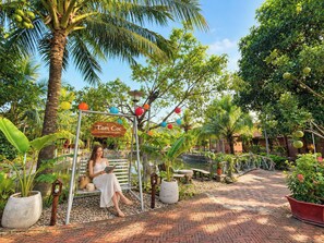 A woman sitting on a swing in a garden with a sign that reads 'Tam Coc Green Garden Bungalows.'