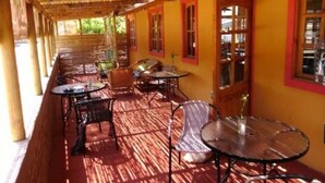 A covered outdoor seating area with tables and chairs, a thatched roof, and yellow walls with red trim. - Cabañas Los Tamarugos (Los Vilos)