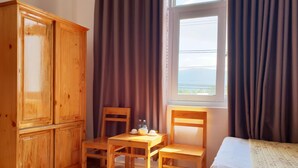 A room with a wooden cabinet, a table with chairs, a bed, and a window with curtains. - Phu Tai Center Hotel (Quy Nhon Tay)