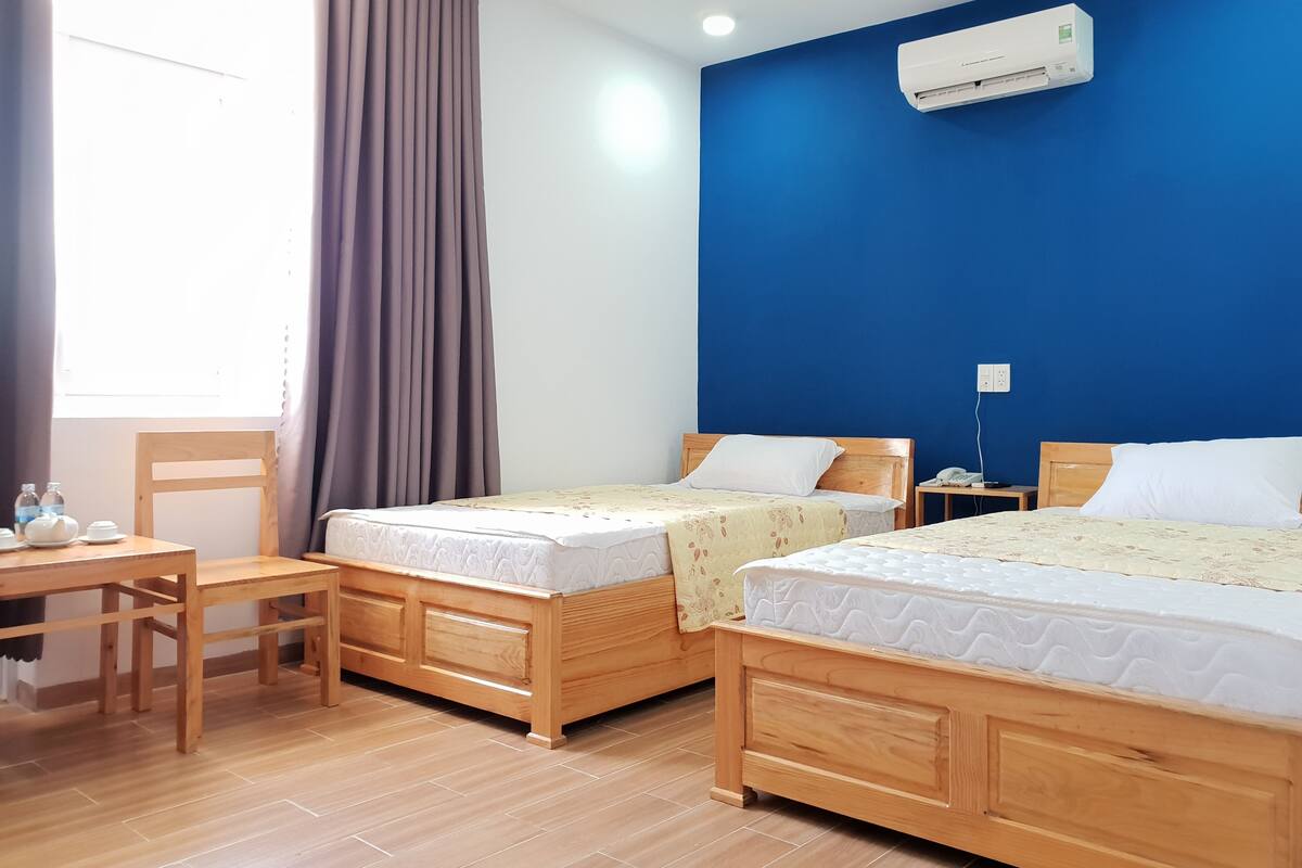 A hotel room with two wooden beds, a desk, a chair, and an air conditioning unit on the wall.