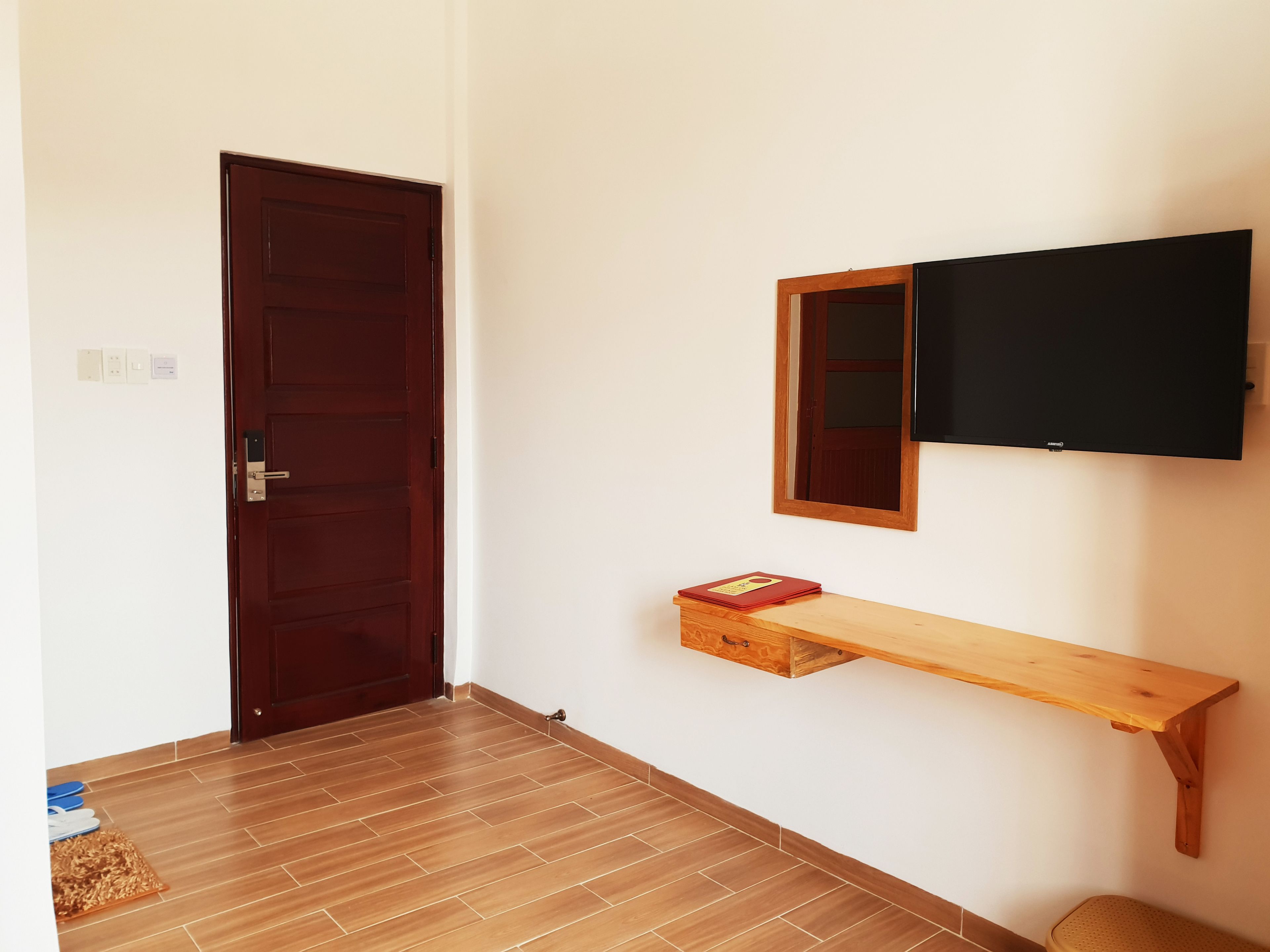 A room with a wooden door, a mounted TV, a wooden shelf, and a patterned floor.
