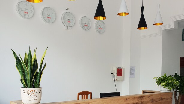 A reception desk with a wooden top and white base, surrounded by white walls and multiple clocks. - Phu Tai Center Hotel (Quy Nhon Tay)