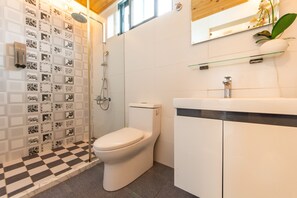Une salle de bain avec un carrelage à motifs géométriques, des toilettes, une douche, un lavabo et un miroir.