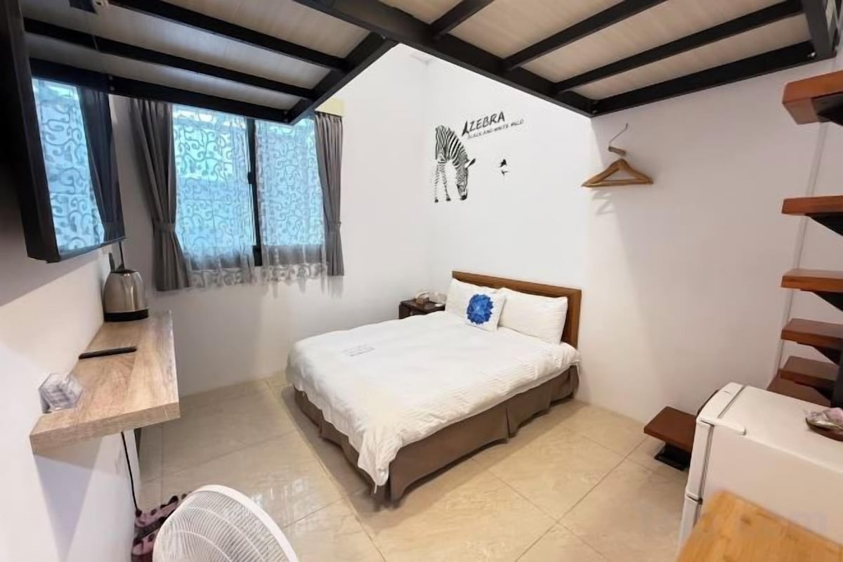 Un dormitorio con cama, escritorio, silla, lámpara colgante y ventana con cortinas.