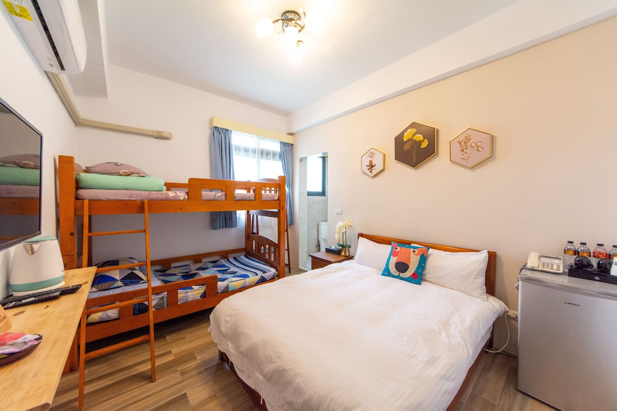A room with bunk beds, a desk with a computer, a refrigerator, and a bedside table with a lamp.