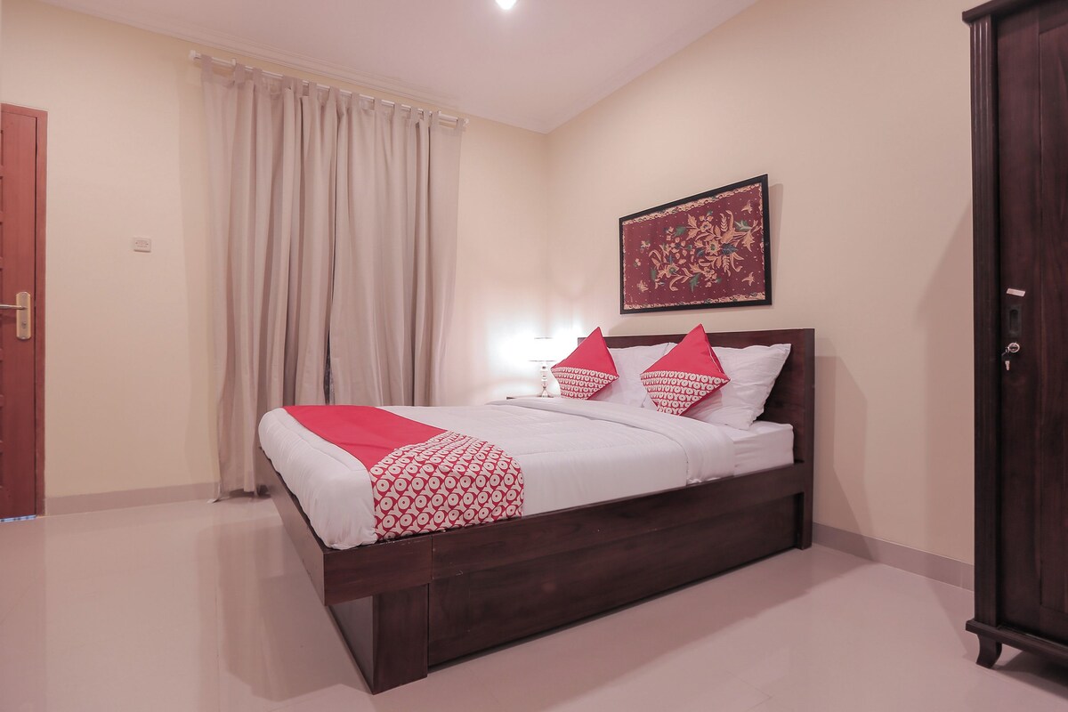 Un lit bien fait, avec une couvre-lit et des oreillers aux motifs rouges et blancs, une tête de lit en bois et une décoration murale au-dessus.