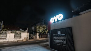 Una entrada con reja y un letrero 'oyo', un muro de concreto y un portón met álico con diseños decorativos.