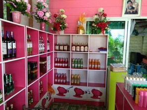 A room with pink walls, shelves stocked with various bottles, and a window with a view. - Ton Tawan resort (Ko Kood)